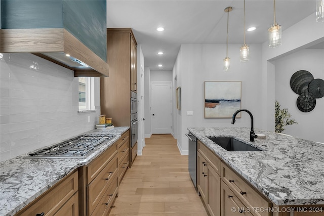 kitchen with light stone countertops, appliances with stainless steel finishes, wall chimney range hood, sink, and light hardwood / wood-style floors