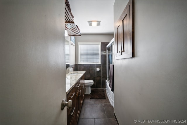 full bathroom with tile walls, shower / bath combination with glass door, toilet, vanity, and tile patterned floors