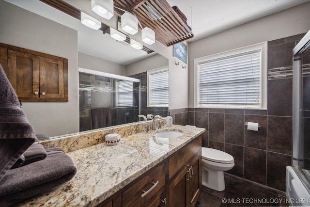 full bathroom with toilet, bath / shower combo with glass door, vanity, and tile walls