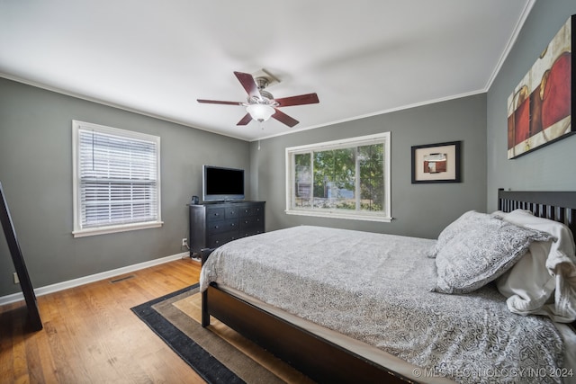 bedroom featuring ceiling fan, crown molding, wood-type flooring, and multiple windows