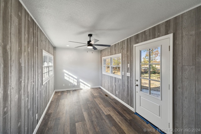 interior space with ceiling fan, dark wood-type flooring, a textured ceiling, and wood walls