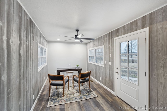 dining area featuring ceiling fan, dark wood-type flooring, a textured ceiling, and wooden walls