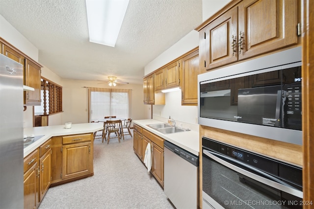 kitchen with kitchen peninsula, appliances with stainless steel finishes, a textured ceiling, light colored carpet, and sink