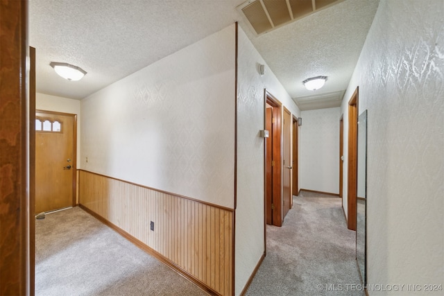 hall with wood walls, a textured ceiling, and light colored carpet