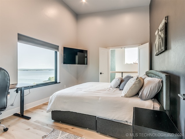 bedroom featuring light hardwood / wood-style floors, a towering ceiling, and multiple windows