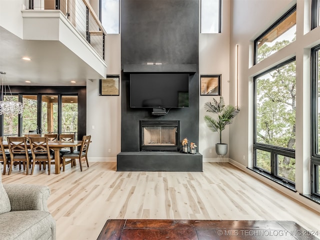 living room featuring a healthy amount of sunlight, a large fireplace, wood-type flooring, and a towering ceiling