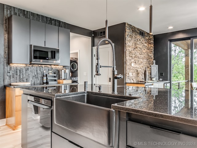 kitchen with stacked washer / dryer, appliances with stainless steel finishes, dark stone counters, and pendant lighting