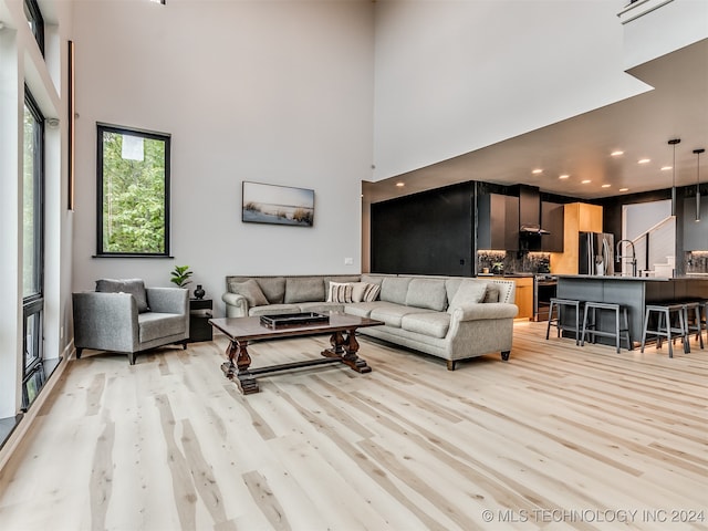 living room with a towering ceiling, sink, and light wood-type flooring