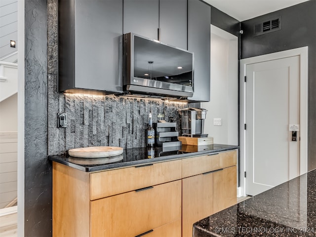 kitchen featuring light brown cabinetry, decorative backsplash, light hardwood / wood-style floors, and dark stone countertops