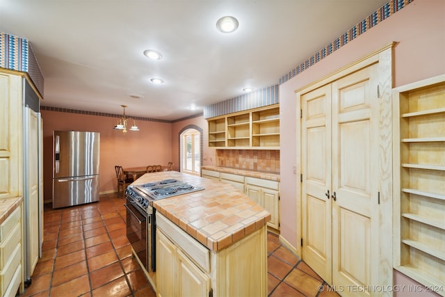 kitchen featuring black range, a center island, hanging light fixtures, stainless steel fridge, and tile counters