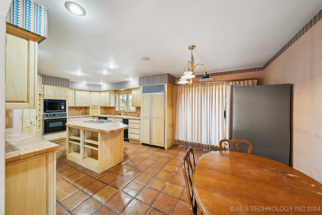 kitchen with black appliances, a center island, hanging light fixtures, and tile counters