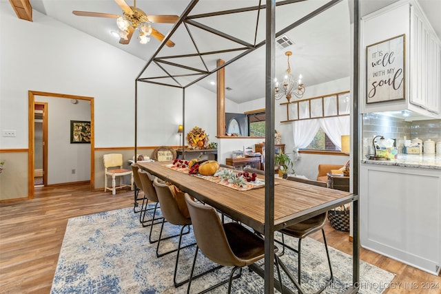 dining area featuring lofted ceiling, ceiling fan with notable chandelier, and light wood-type flooring