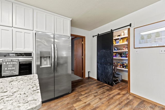 kitchen with appliances with stainless steel finishes, a barn door, white cabinets, dark wood-type flooring, and light stone counters