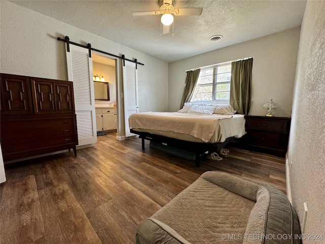 bedroom featuring ensuite bath, dark wood-type flooring, ceiling fan, a textured ceiling, and a barn door