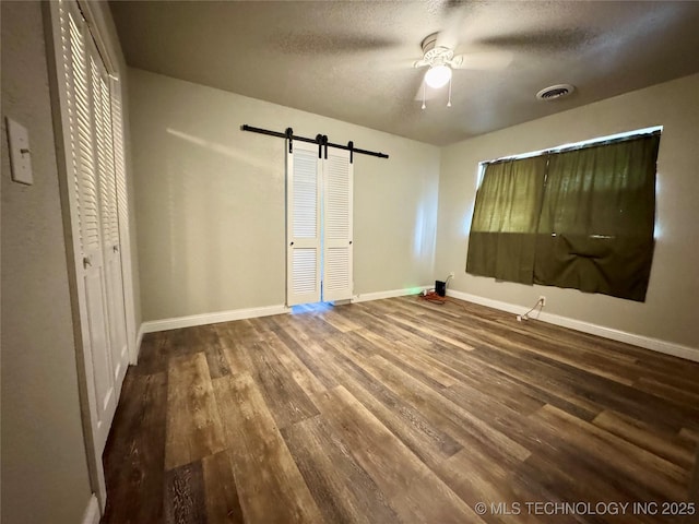 unfurnished bedroom featuring ceiling fan, wood-type flooring, a textured ceiling, a barn door, and a closet