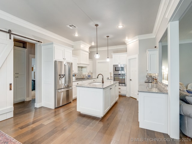 kitchen featuring white cabinets, appliances with stainless steel finishes, a barn door, pendant lighting, and light hardwood / wood-style floors