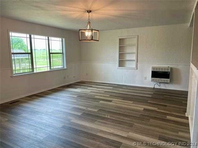 unfurnished room with dark hardwood / wood-style floors, a chandelier, heating unit, and built in shelves