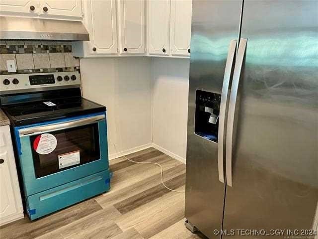 kitchen with decorative backsplash, white cabinetry, light hardwood / wood-style flooring, and stainless steel appliances