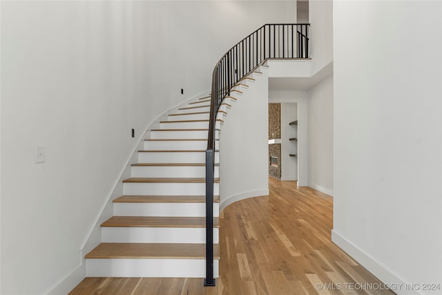 staircase featuring wood-type flooring and a brick fireplace