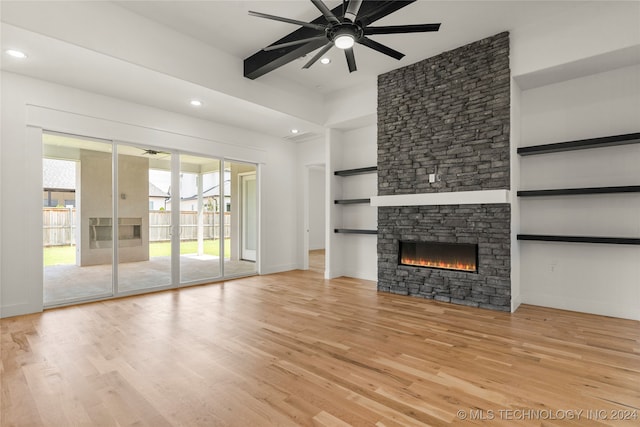 unfurnished living room with a stone fireplace, built in features, light wood-type flooring, and ceiling fan