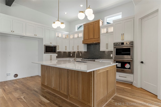 kitchen featuring a center island with sink, sink, white cabinetry, light wood-type flooring, and appliances with stainless steel finishes