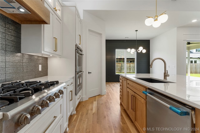 kitchen with white cabinets, hanging light fixtures, appliances with stainless steel finishes, light wood-type flooring, and a notable chandelier