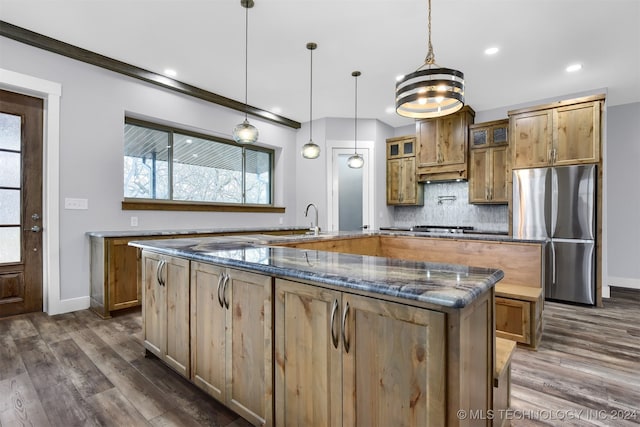 kitchen featuring dark wood-type flooring, dark stone counters, tasteful backsplash, stainless steel refrigerator, and pendant lighting