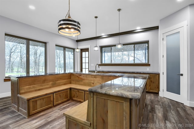 kitchen featuring hanging light fixtures, light stone countertops, dark hardwood / wood-style floors, and sink