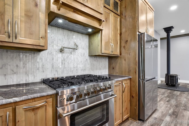 kitchen with stainless steel appliances, a wood stove, hardwood / wood-style flooring, custom exhaust hood, and stone counters