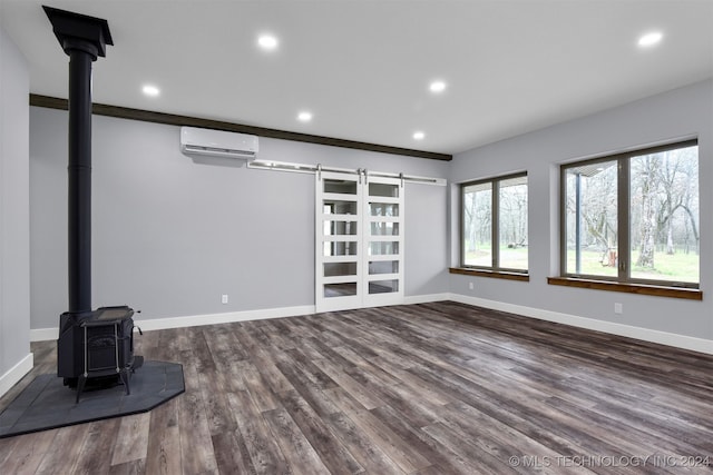 unfurnished living room with a barn door, wood-type flooring, a wood stove, and a wall mounted air conditioner