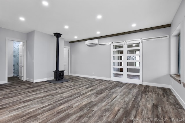 unfurnished living room with dark hardwood / wood-style flooring, a wall mounted AC, a barn door, and a wood stove