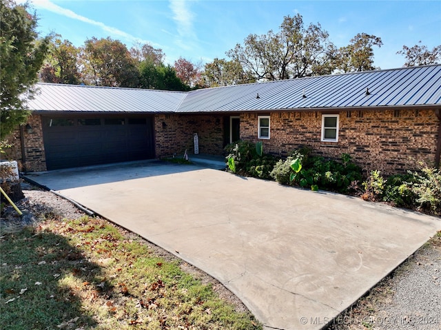 ranch-style home with driveway, metal roof, an attached garage, a standing seam roof, and brick siding