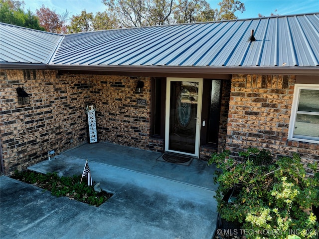 doorway to property with stone siding, brick siding, metal roof, and a patio