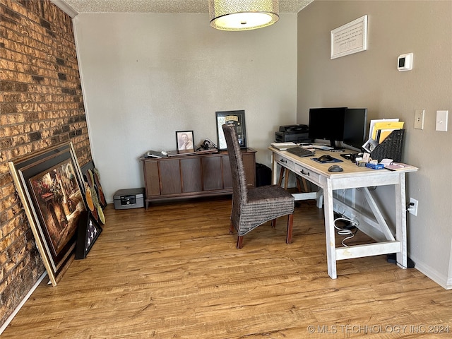 home office with brick wall, a textured ceiling, light wood-type flooring, and a fireplace