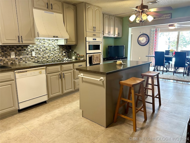 kitchen with white appliances, a textured ceiling, a center island, a kitchen breakfast bar, and ceiling fan