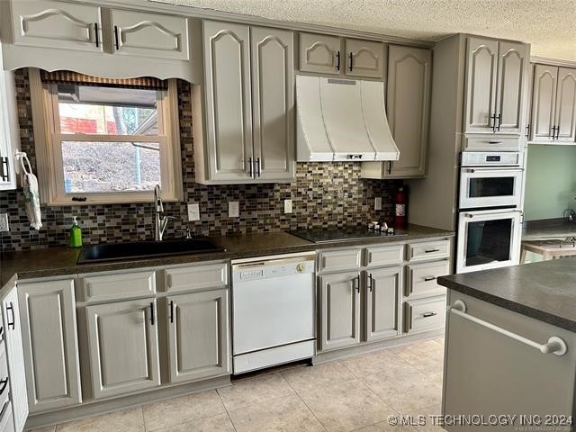 kitchen featuring decorative backsplash, light tile patterned floors, sink, ventilation hood, and white appliances