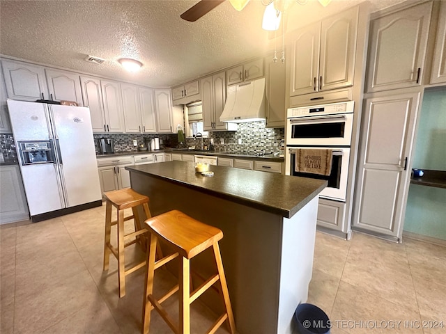 kitchen featuring a breakfast bar area, light tile patterned floors, backsplash, a textured ceiling, and white appliances