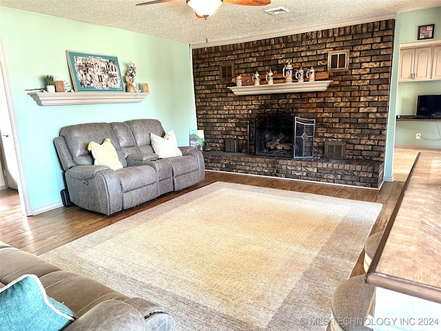 living room with a textured ceiling, hardwood / wood-style flooring, ceiling fan, and a brick fireplace