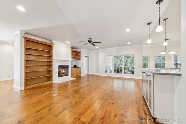 unfurnished living room with ceiling fan, ornamental molding, and light wood-type flooring