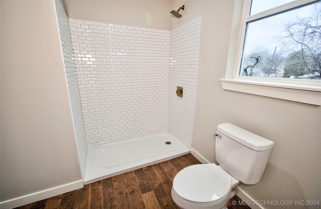 bathroom with a tile shower, toilet, and wood-type flooring