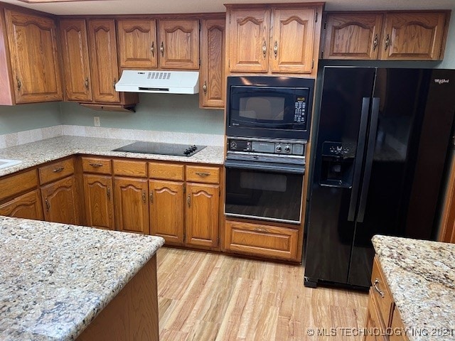 kitchen featuring light stone counters, black appliances, and light wood-type flooring