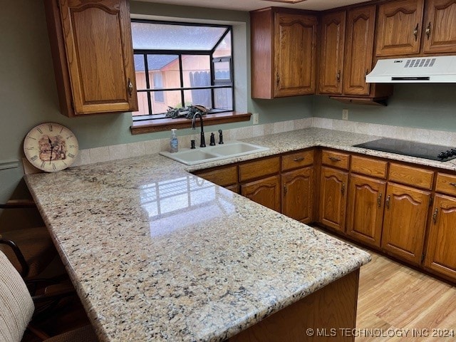 kitchen with black electric cooktop, range hood, sink, light stone counters, and light hardwood / wood-style floors