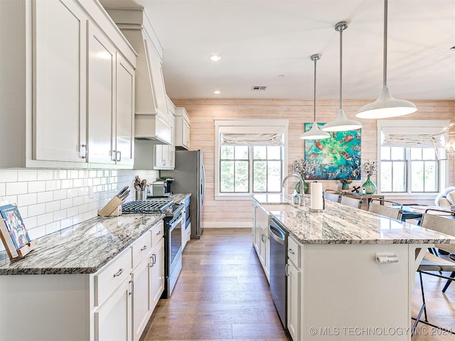 kitchen with appliances with stainless steel finishes, decorative light fixtures, a healthy amount of sunlight, and wooden walls