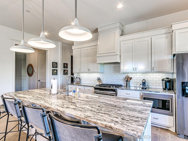 kitchen with appliances with stainless steel finishes, hanging light fixtures, white cabinets, and an island with sink