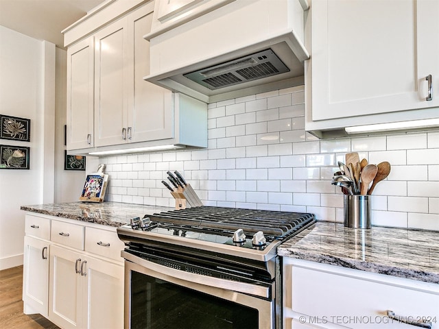 kitchen featuring dark stone countertops, white cabinetry, gas stove, light hardwood / wood-style floors, and tasteful backsplash