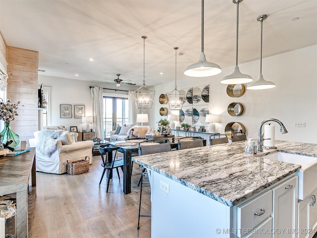 kitchen with decorative light fixtures, white cabinets, light stone counters, light hardwood / wood-style floors, and ceiling fan