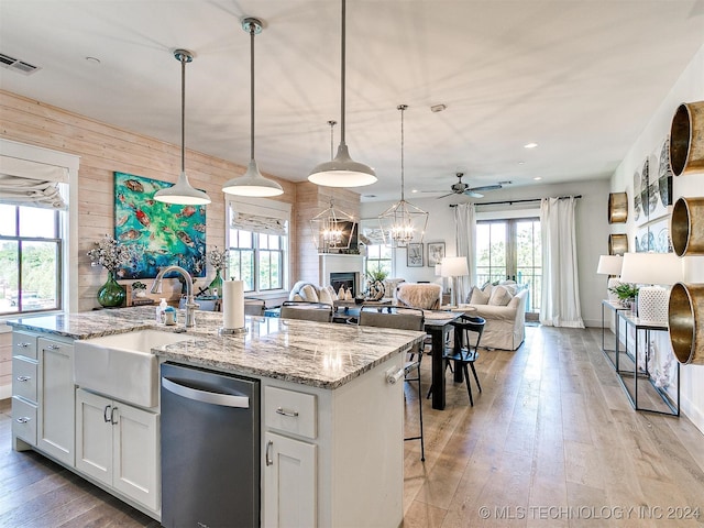 kitchen with an island with sink, white cabinetry, ceiling fan with notable chandelier, pendant lighting, and wooden walls