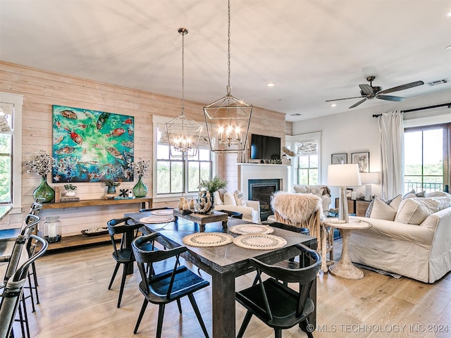 dining space featuring wooden walls, ceiling fan with notable chandelier, and light hardwood / wood-style floors