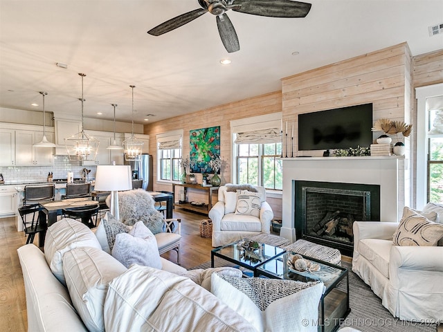 living room featuring wooden walls, light hardwood / wood-style flooring, ceiling fan with notable chandelier, and plenty of natural light