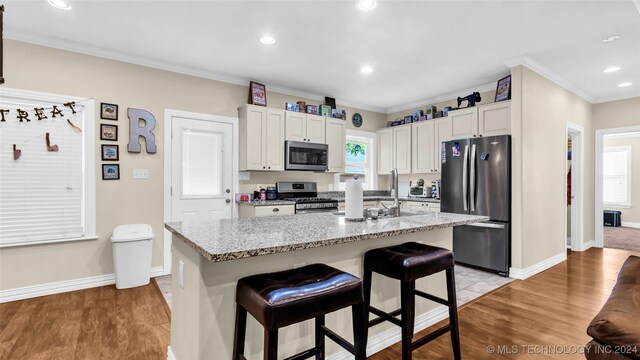 kitchen with a breakfast bar area, appliances with stainless steel finishes, light hardwood / wood-style floors, and an island with sink